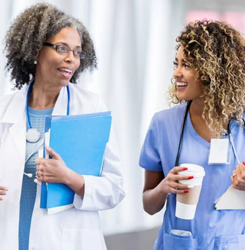 Female doctor chatting with a nurse holding a coffee cup