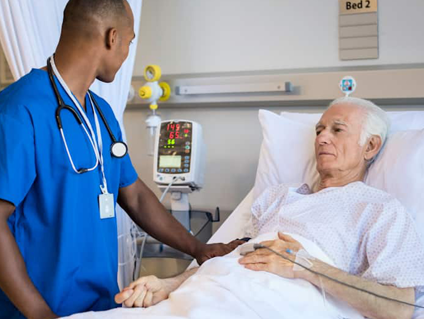 Male nurse standing by an elderly male patient in bed