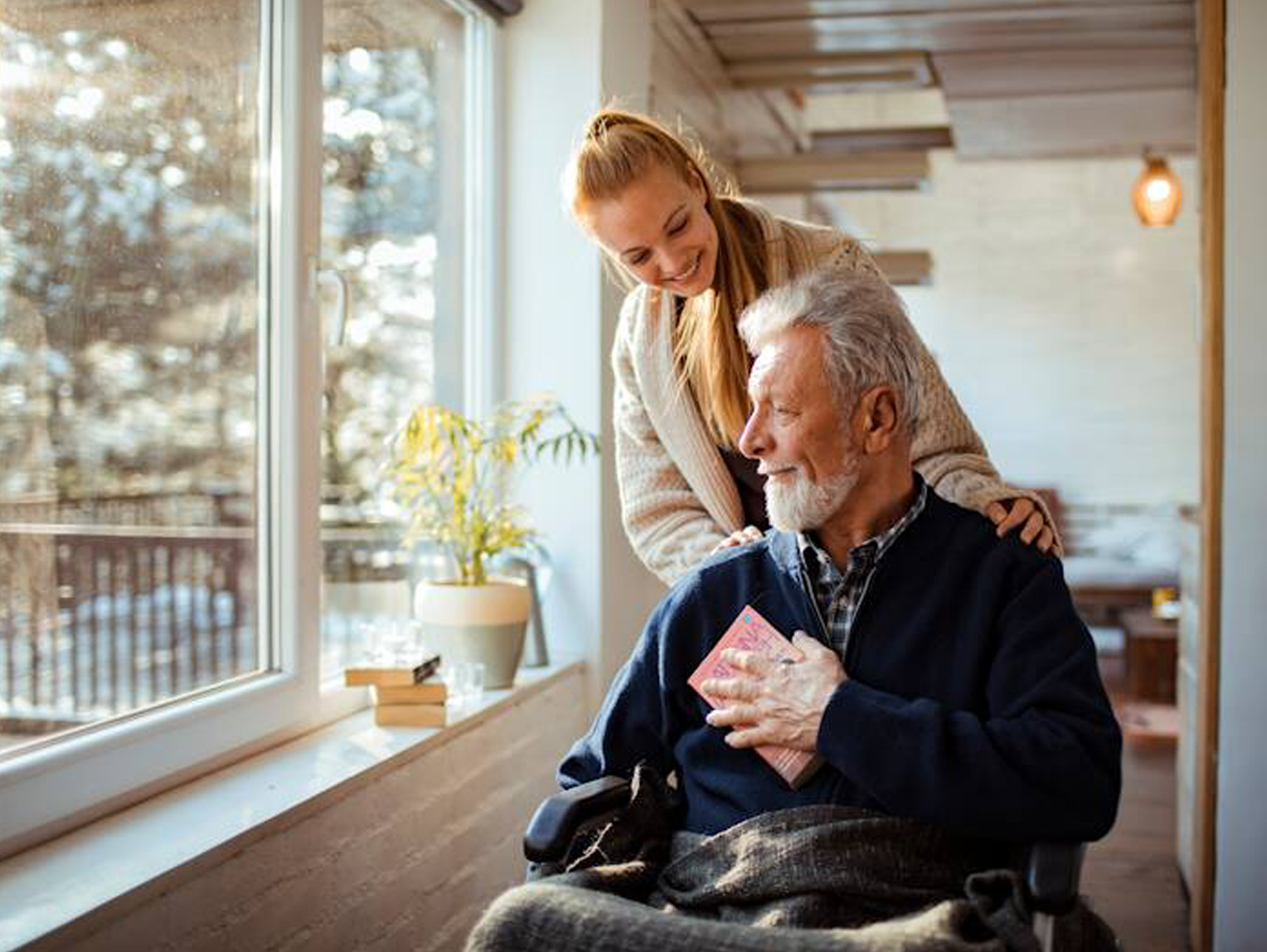 A young woman standing behind an old man on a wheelchair