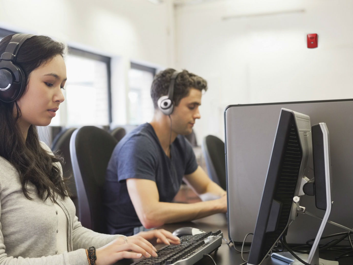 People wearing headphones sitting at desks working on their desktops