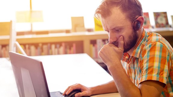 Man with headphones on intensely focusing on laptop screen