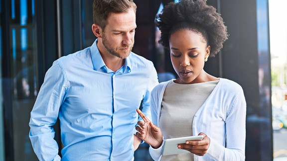 A woman talking to a man as they look at the screen of a tablet