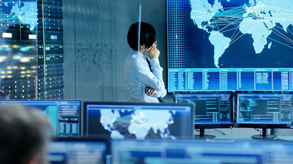 Person in a control room looking at a large screen with the world map
