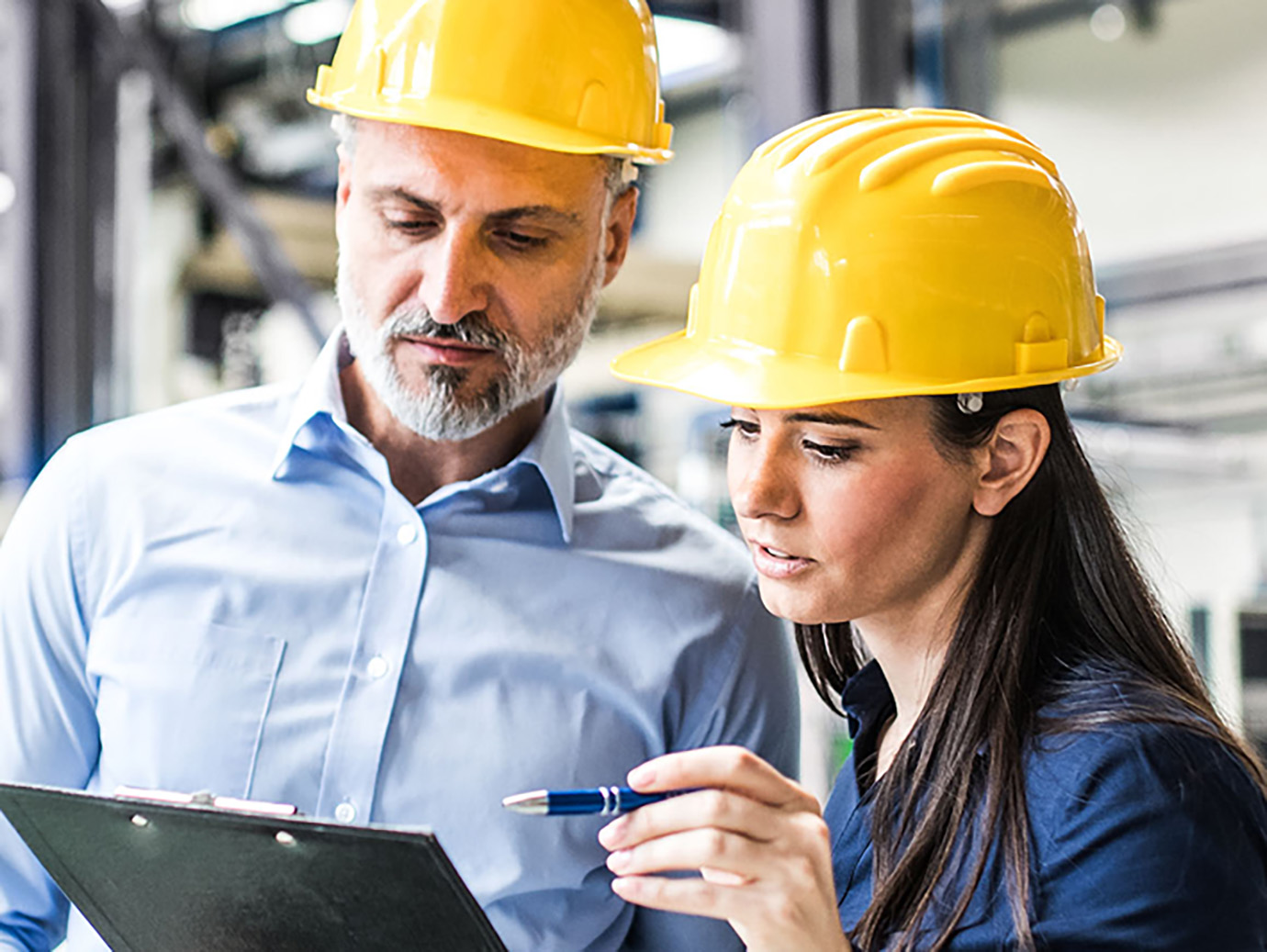 Two people in a safety hat conversing looking at a clipboard 