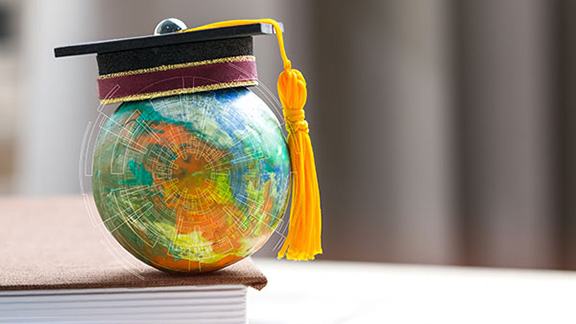A miniature globe with a graduation hat stacked on a book