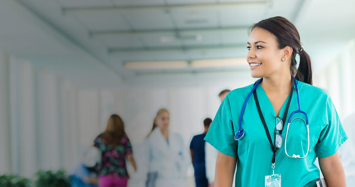 A medical professional in scrubs smiling with a stethoscope around her neck