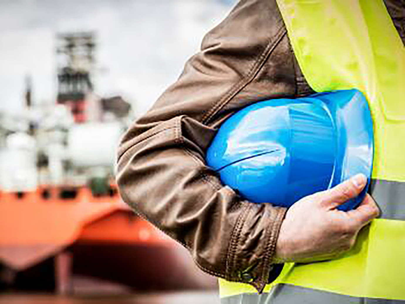 Man in uniform holding a blue safety helmet in front of a ship