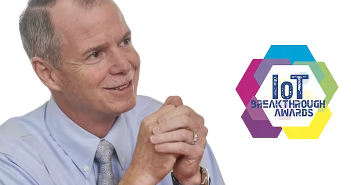 George Oliver, Chairman & CEO of Johnson Controls, smiling; logo of the IoT Breakthrough Awards overlaid