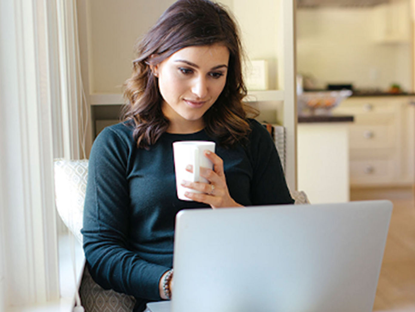 Woman holding a coffee mug while working on a laptop