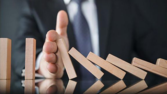 A businessman holding his hand to stop a row of wodden domino tiles from falling