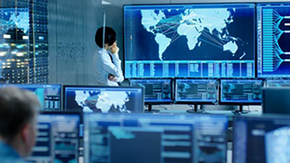 A man looking at maps displayed on a screen, surrounded by computers