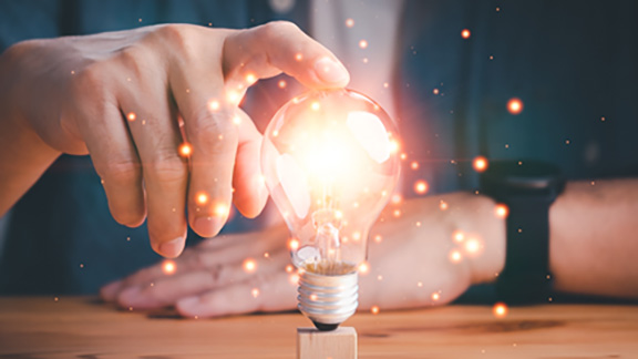 A man holding a lit-up lightbulb on a table