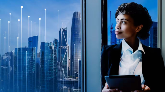 Female employee looking out of a window overlooking a cityscape, overlaid with a modern graphic