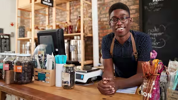 A barista leaning over a cafe counter smiling at the camera