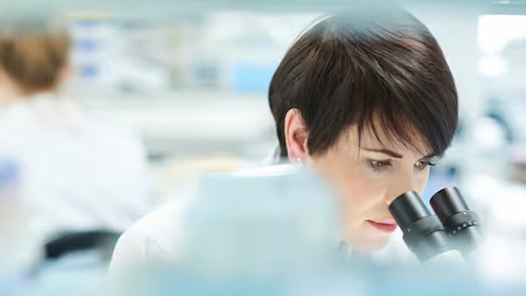 Close-up of a woman in a laboratory looking through a microscope