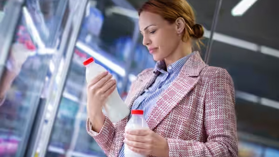 Woman holding two bottles of milk in front of a dairy fridge at a supermarket