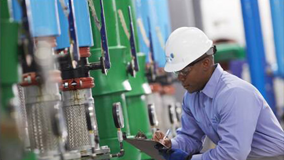 Man in safety equipment kneeling inspecting a machine through a tablet
