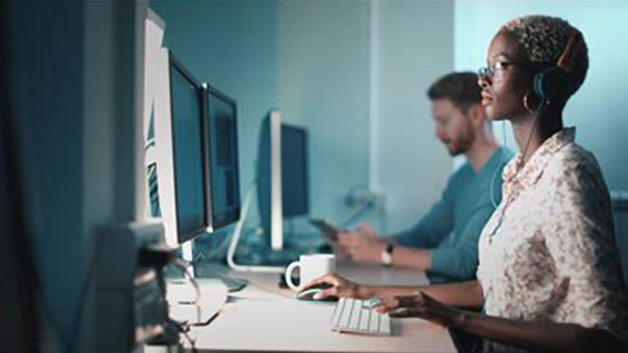 Two people working in front of a desktop at a desk