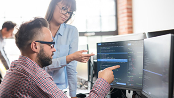 Two corporate employees examining code displayed on a desktop