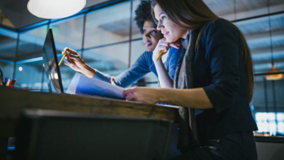 Two female employees working on a laptop, while one of them points at the screen