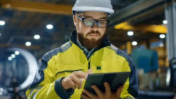 A person wearing a hard hat and glasses holding a tablet