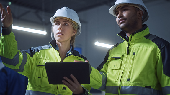A person and person wearing hard hats and working on a tablet