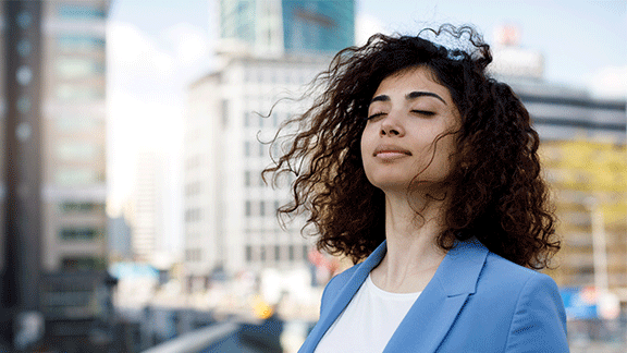 Woman breathing in open air with her eyes closed, with buildings in the background