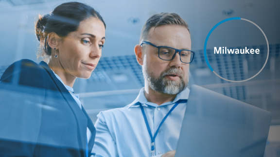 A man showing a woman something on a laptop, overlaid with a line of text reading 'Milwaukee' in the corner