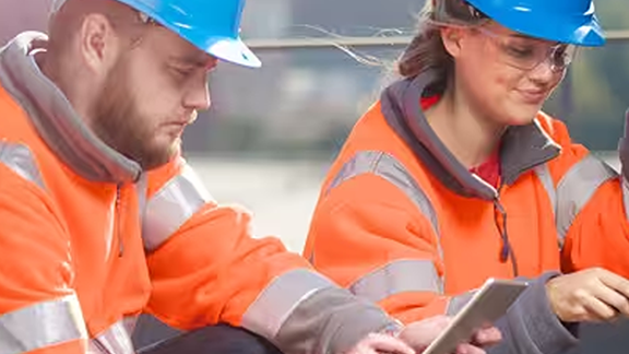 Two maintenance workers kneeling before a device, while one scrolls on a tablet