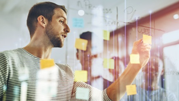 A man looking at a sticky note on a glass wall