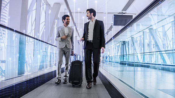 Two men carrying luggage and talking in an airport