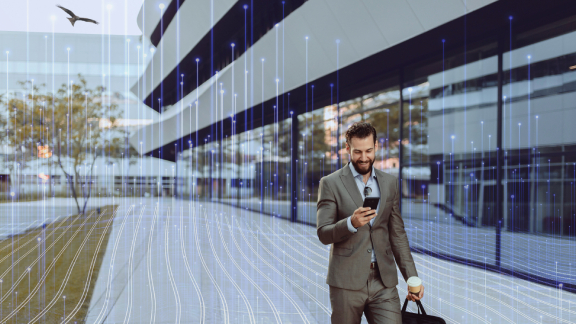 A man looking at his phone and walking along a corporate building, with an eagle flying overhead