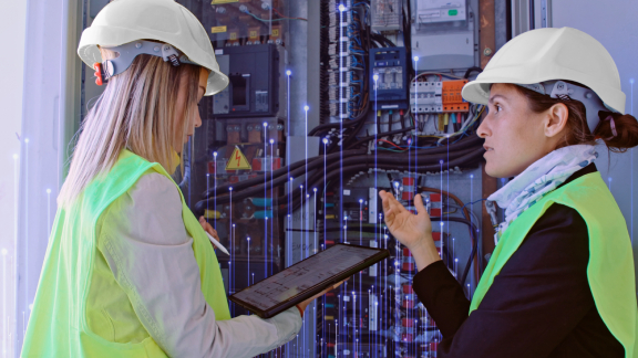 Two female maintenance engineers in front of a device, one of them holding a tablet