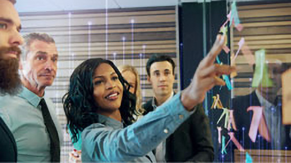 A woman pointing at sticky notes on a glass panel to her colleagues