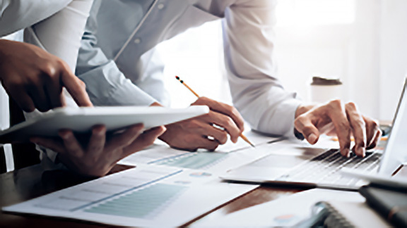 Close-up of two people writing on a document with a pencil